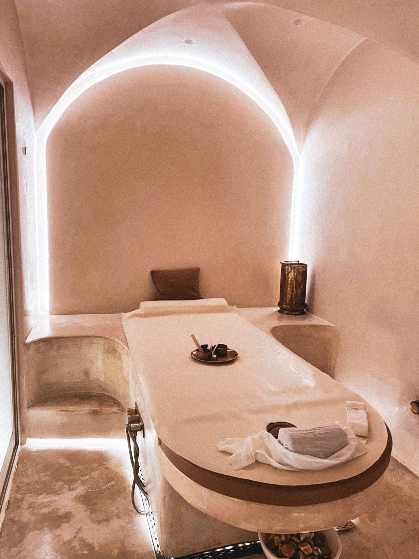 Sala de masaje bajo un arco blanco, con camilla y luz cálida